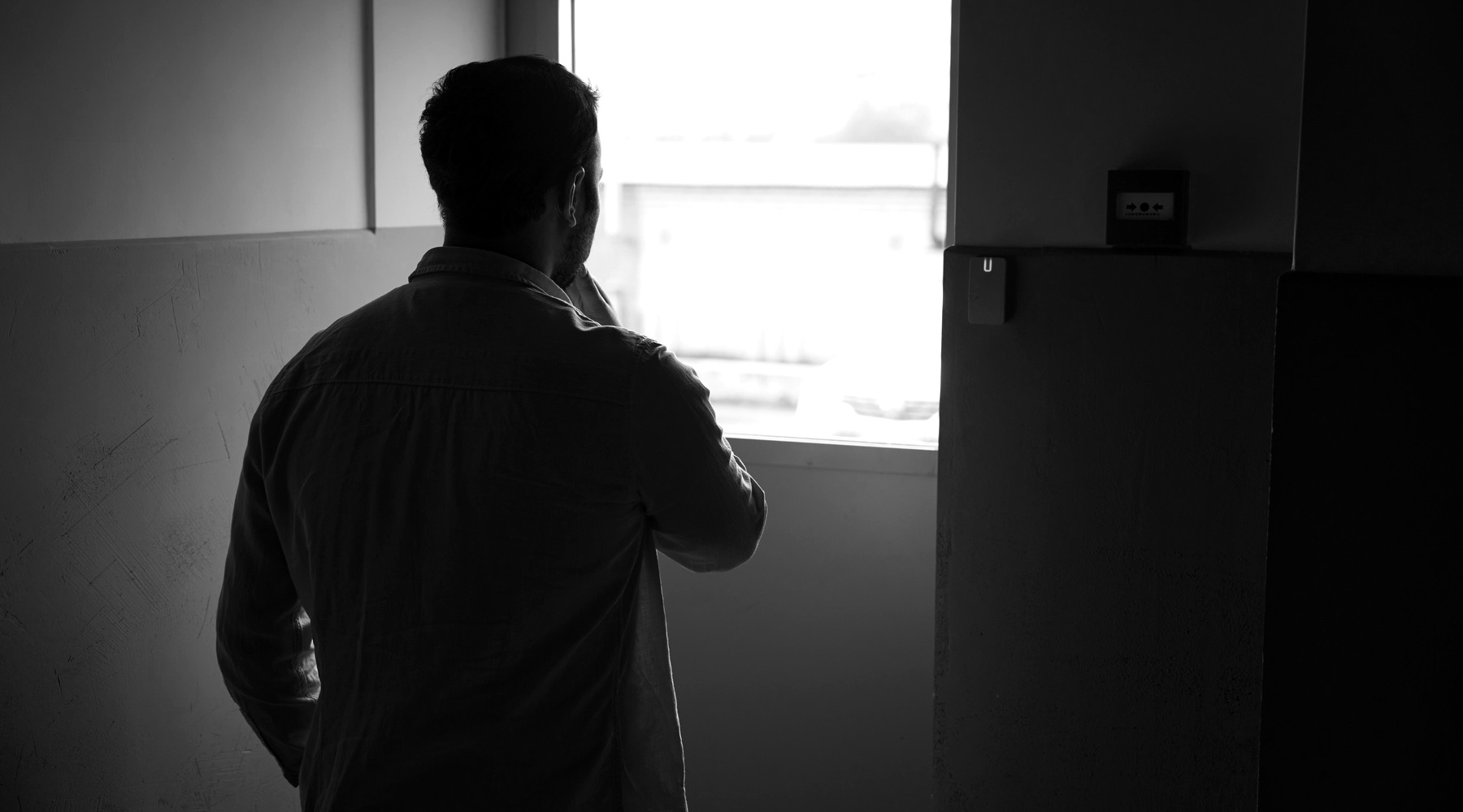 Black-and-white photograph of a person looking out a window.